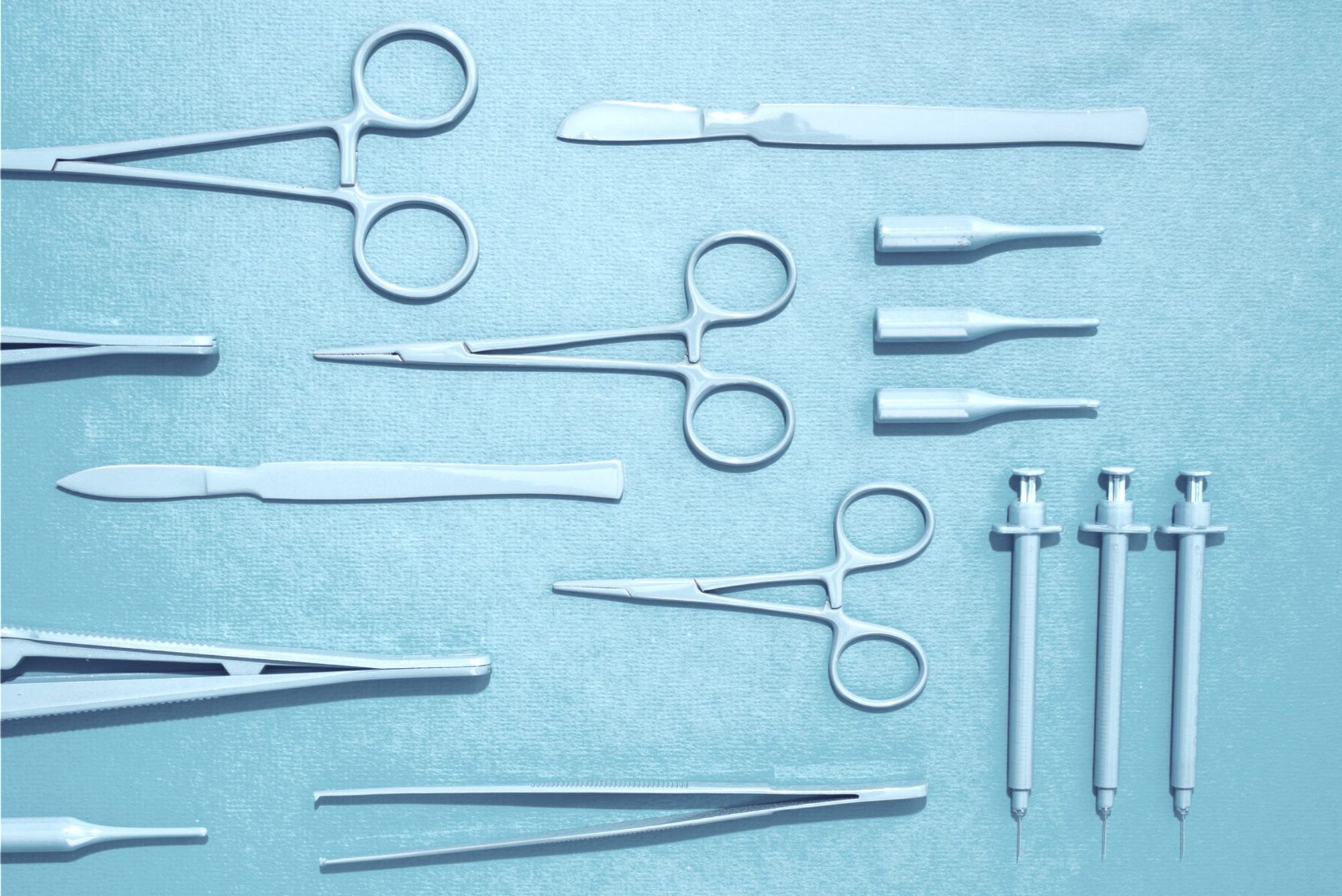Surgical scissors, forceps and scalpels laid out on a pale blue surface