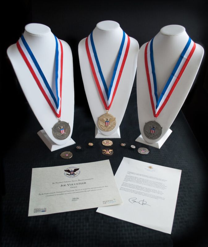Three President's Volunteer Service Award medals on display stands with certificates